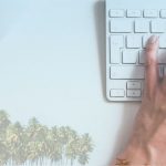 Hands typing on keyboard with palm trees in background