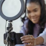 Young woman recording herself with a smartphone on a stand with a ring light on top